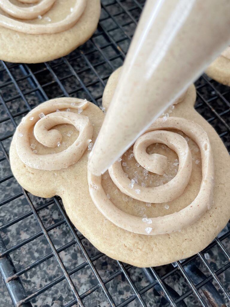 Churro frosting being piped onto a Mickey Churro Sugar Cookie.