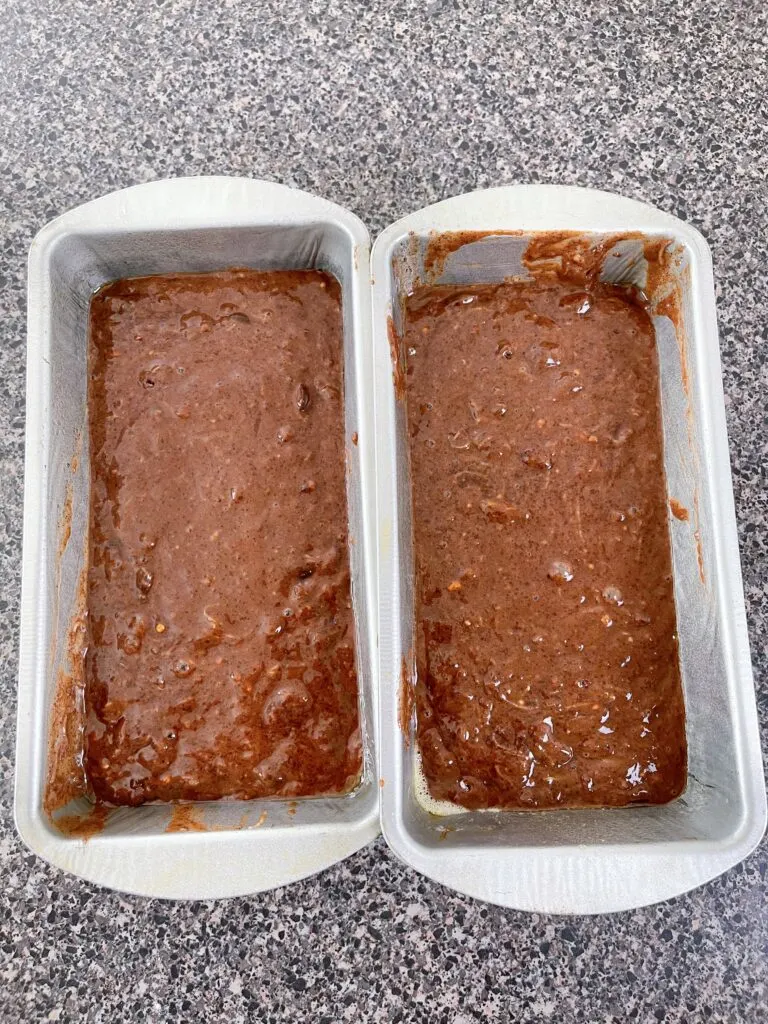 Two loaf pans filled with zucchini bread batter.