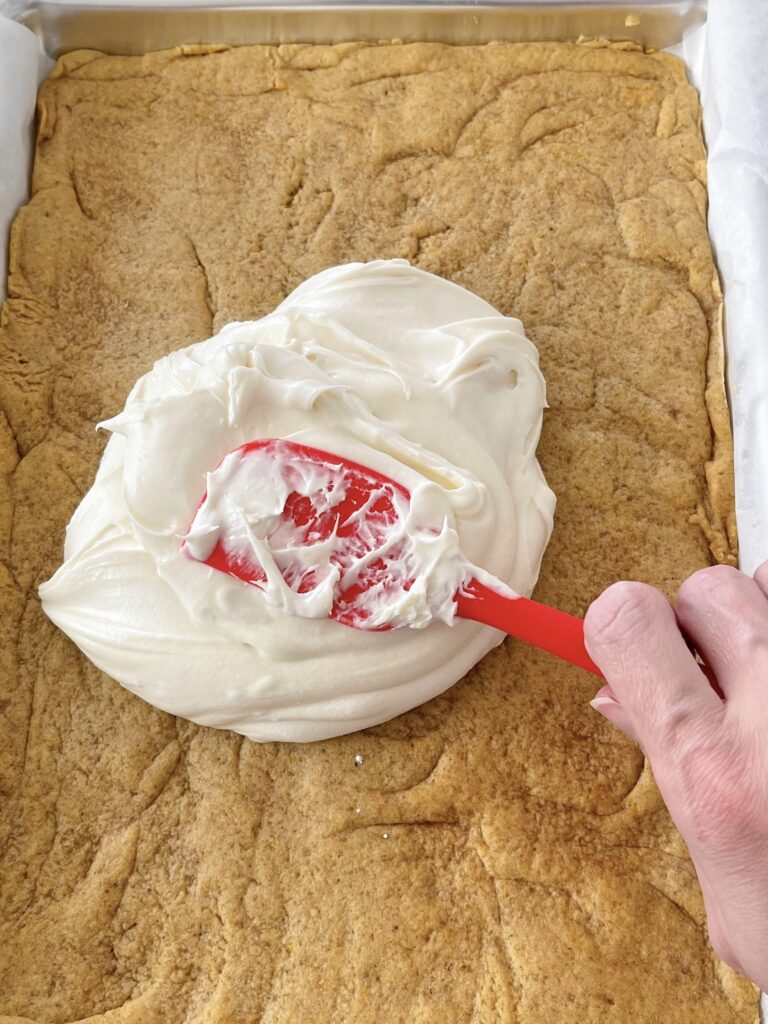 Cream cheese frosting spread over pumpkin sugar cookie bars.