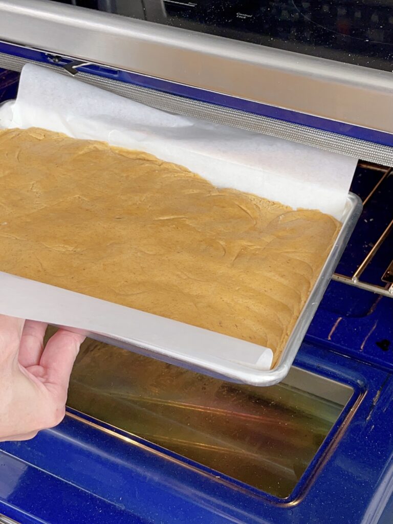 A pan of pumpkin sugar cookie bars being placed in an oven.