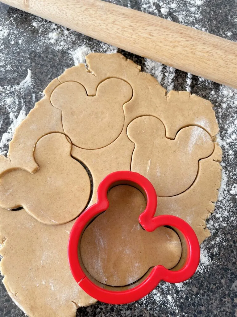 A Mickey mouse cookie cutter with cookie dough.