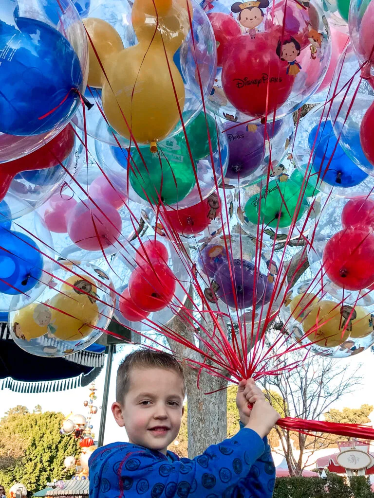 A boy at Disneyland with a bunch of balloons.