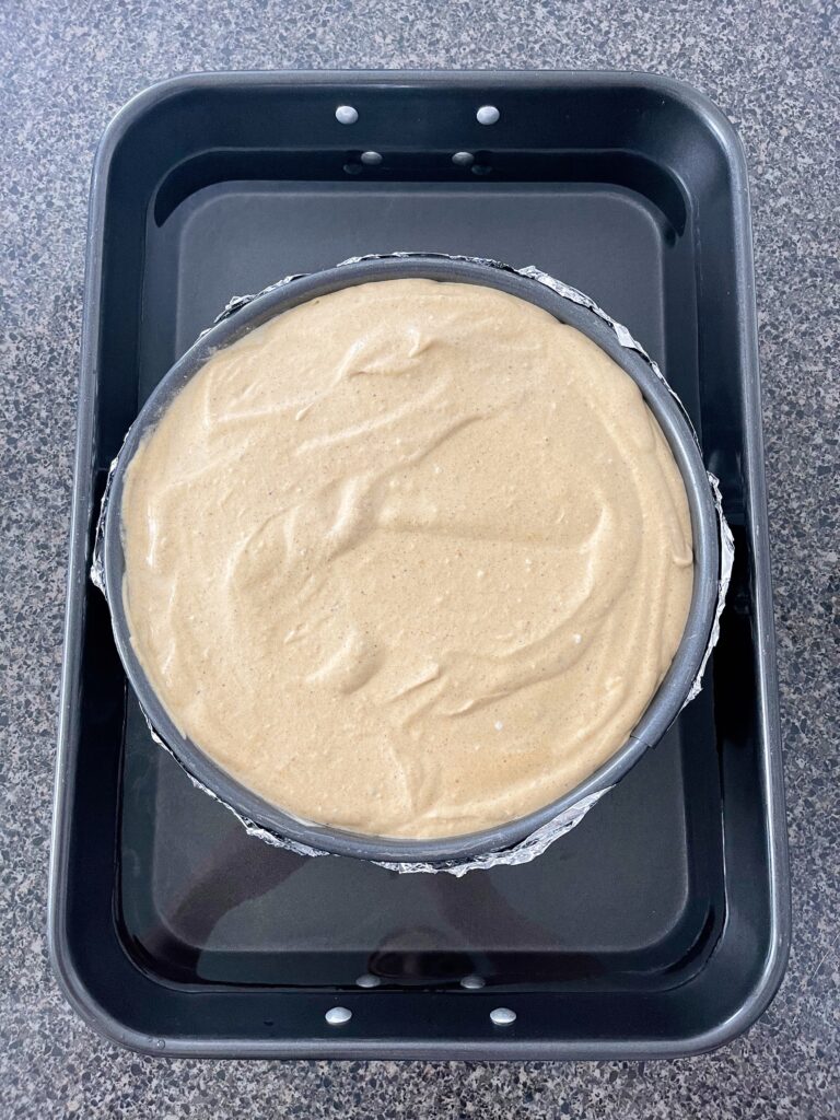 Pumpkin cheesecake batter in a springform pan inside a water bath.