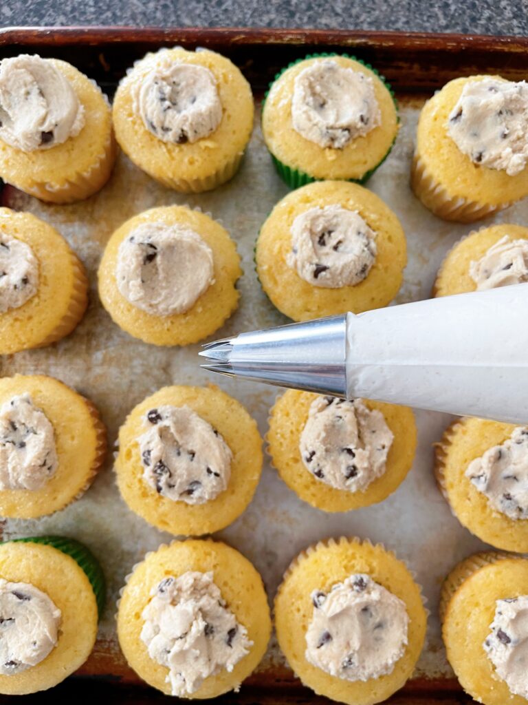 A piping bag filled with frosting and cookie dough stuffed cupcakes.