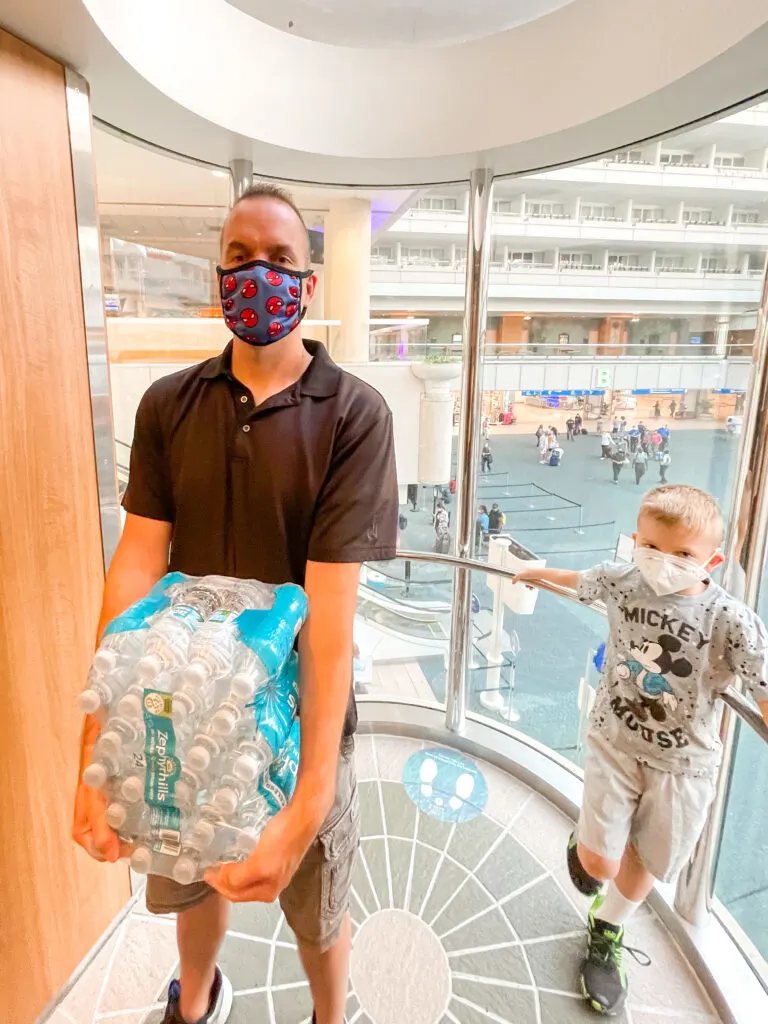 A man and a child holding a case of bottled water to take on a Disney Cruise.