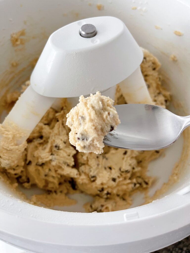 Edible cookie dough on a spoon over a stand mixer.