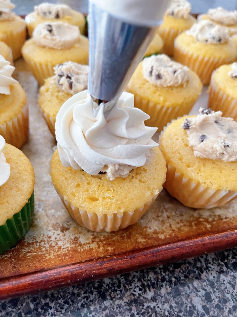 Brown sugar frosting being piped onto a cookie dough cupcake.
