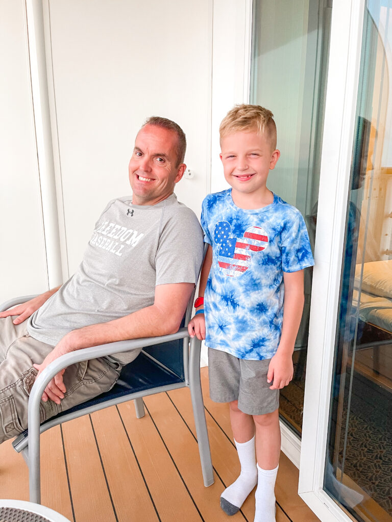 A dad and son sitting on the verandah of the Disney Dream stateroom 8614.
