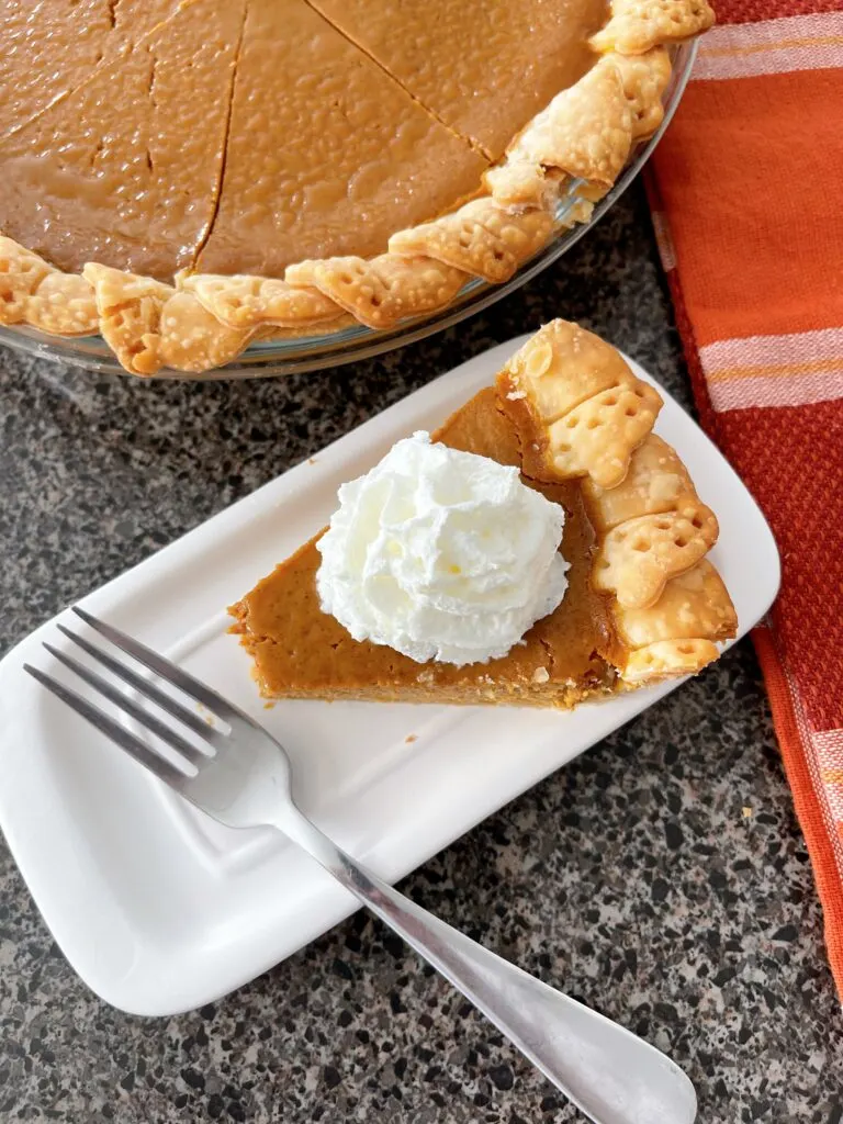 A slice of pumpkin pie with whipped cream and a fork.
