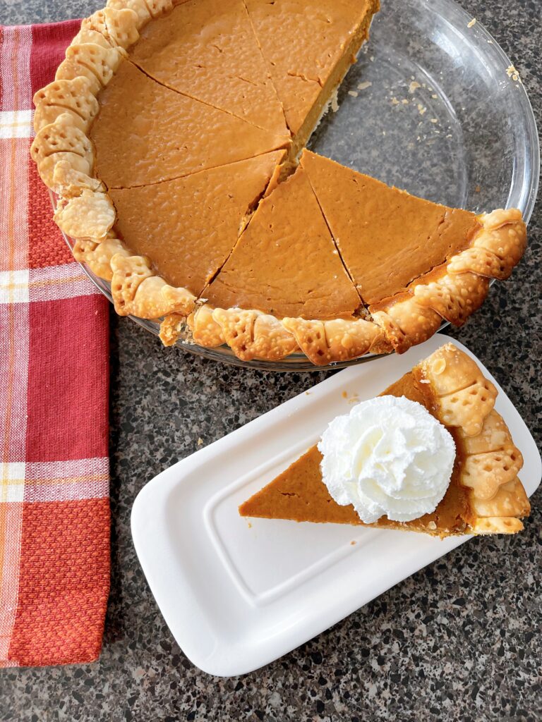 A slice of pumpkin pie next to a pie in a pie plate.