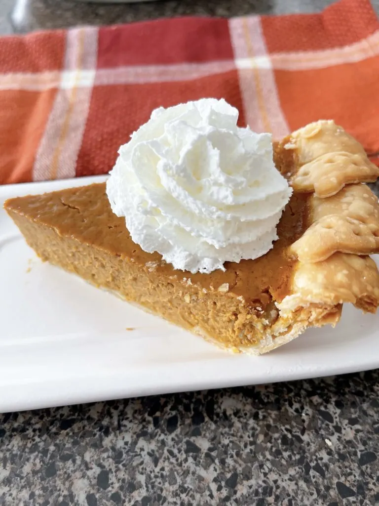 A slice of pumpkin pie with whipped cream on a white plate.