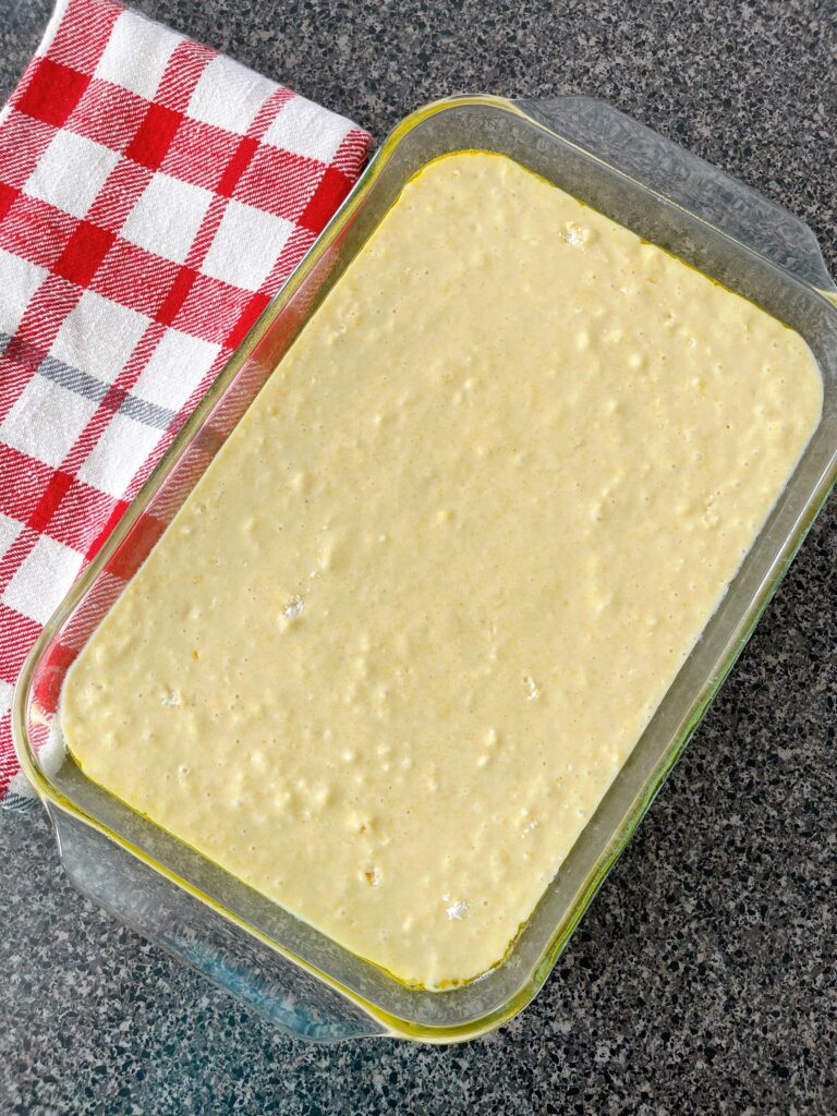 Cornbread batter in a 9x13 pan next to a red and white kitchen towel.