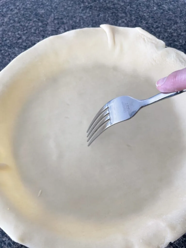 A fork poking a pie crust to prevent bubbles.