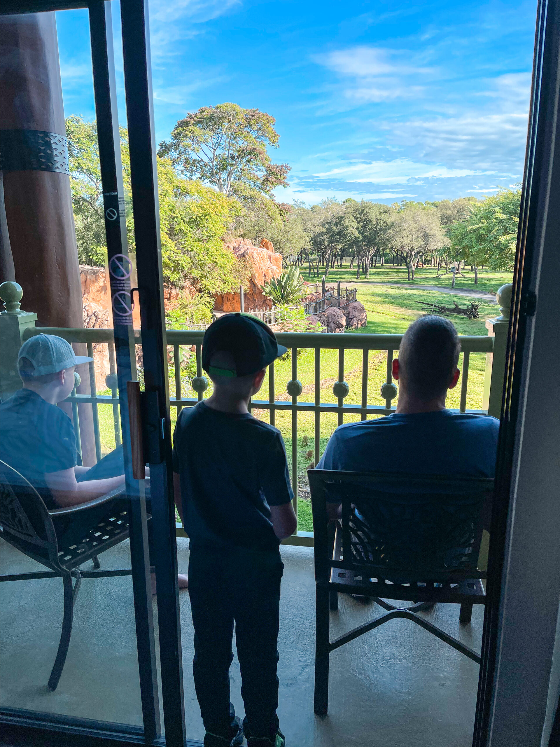 Three people on the balcony of a standard room with a savanna view at Disney's Animal Kingdom Lodge.