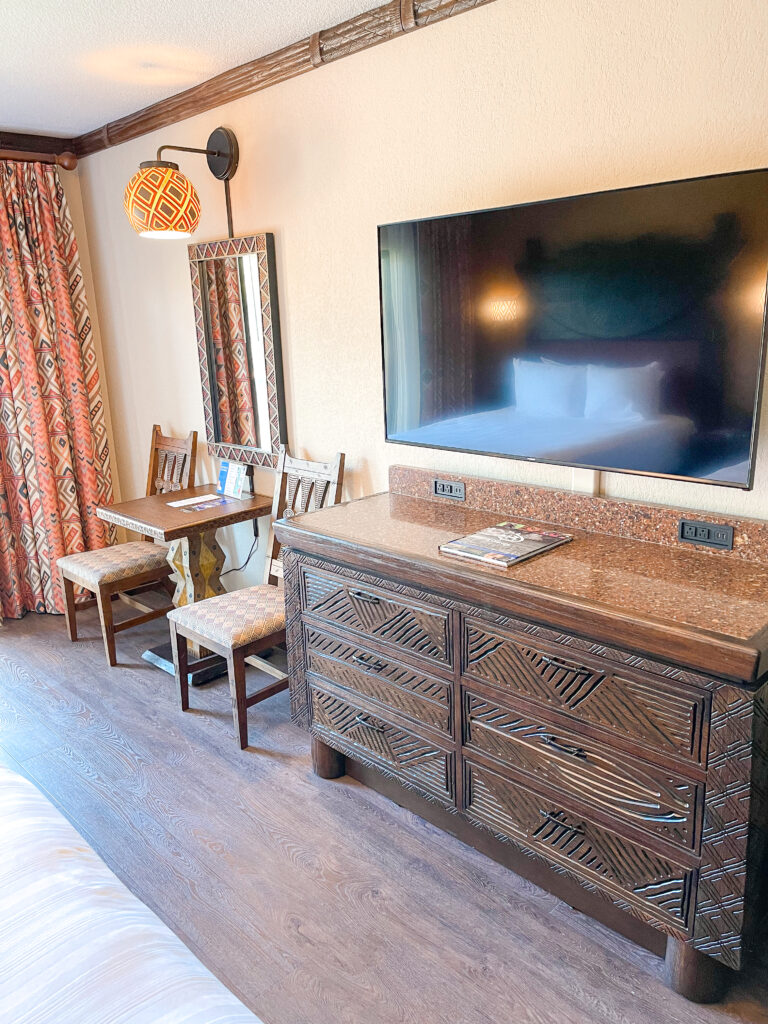 A small table, two chairs, dresser, and a tv in a standard room with a savanna view at Disney's Animal Kingdom Lodge.