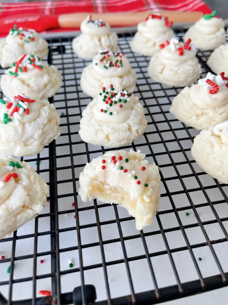 Melt away cookies with cream cheese frosting and Christmas sprinkles on a cooling rack.