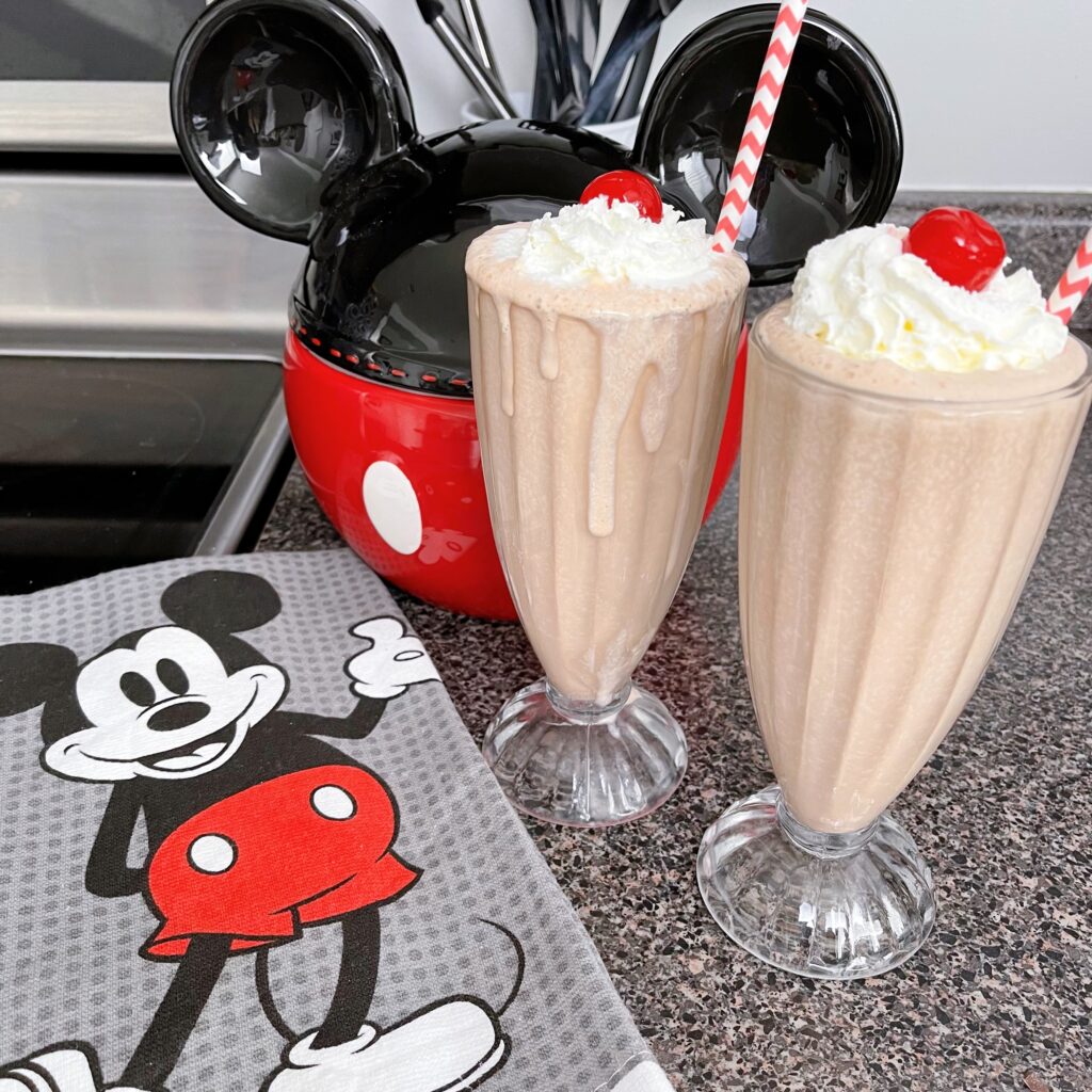 Two cups of chocolate malt with a Mickey Mouse cookie jar and kitchen towel.