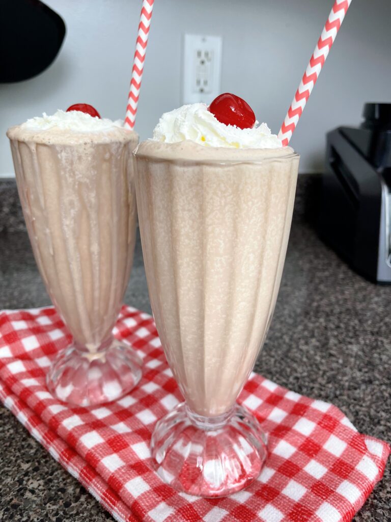 Two chocolate malts with a cherry and a straw.