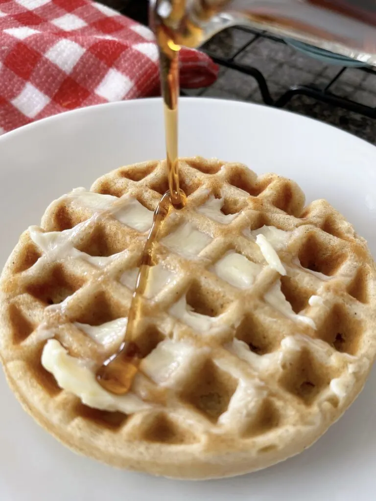 Syrup being drizzled on a waffle covered with butter.