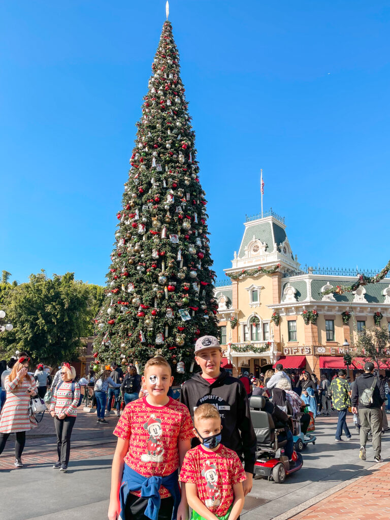 Three kids in front of the Christmas Tree at Disneyland.