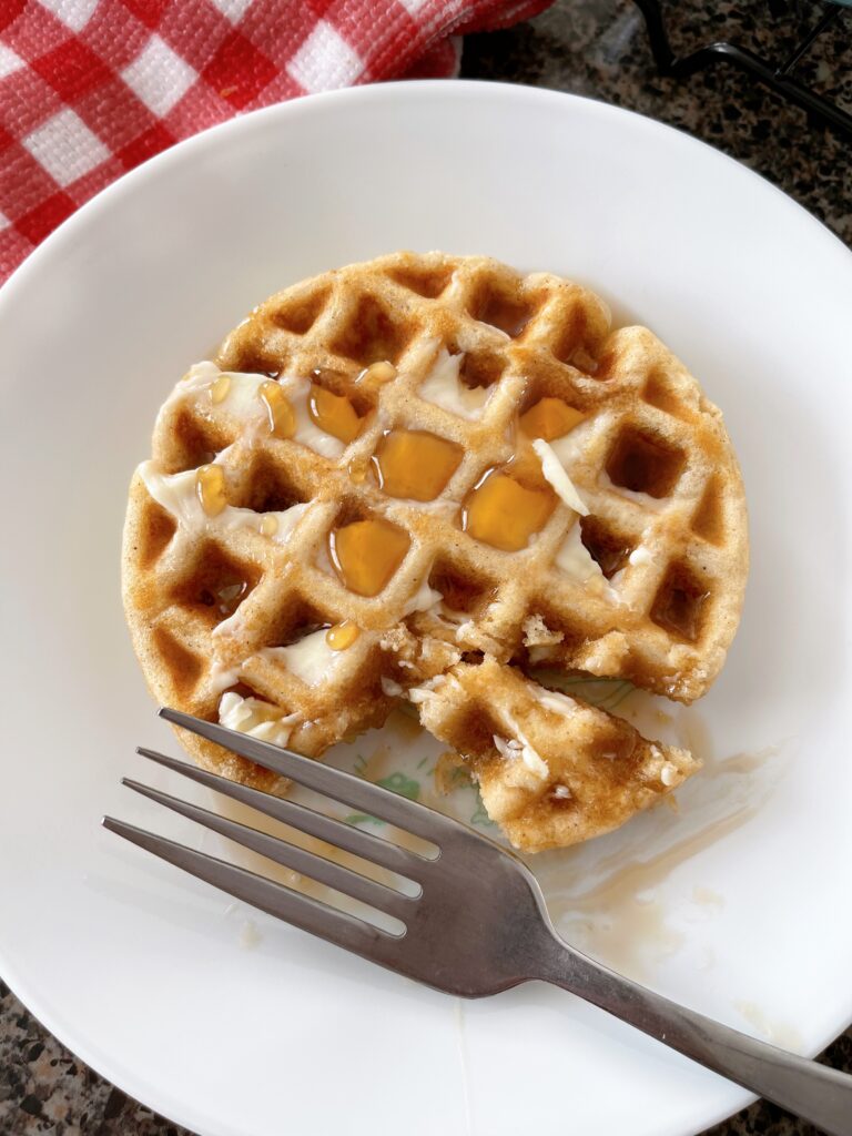 A fork and a waffle covered in syrup and butter on a plate.