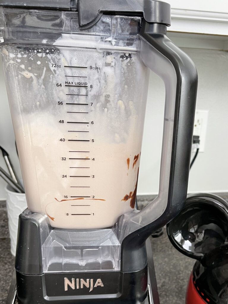 A blender filled with ice cream, chocolate sauce, malted milk, and milk to make a chocolate malt.