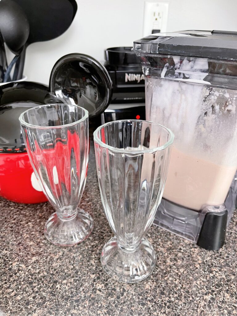 A blender of chocolate malt and two glasses.
