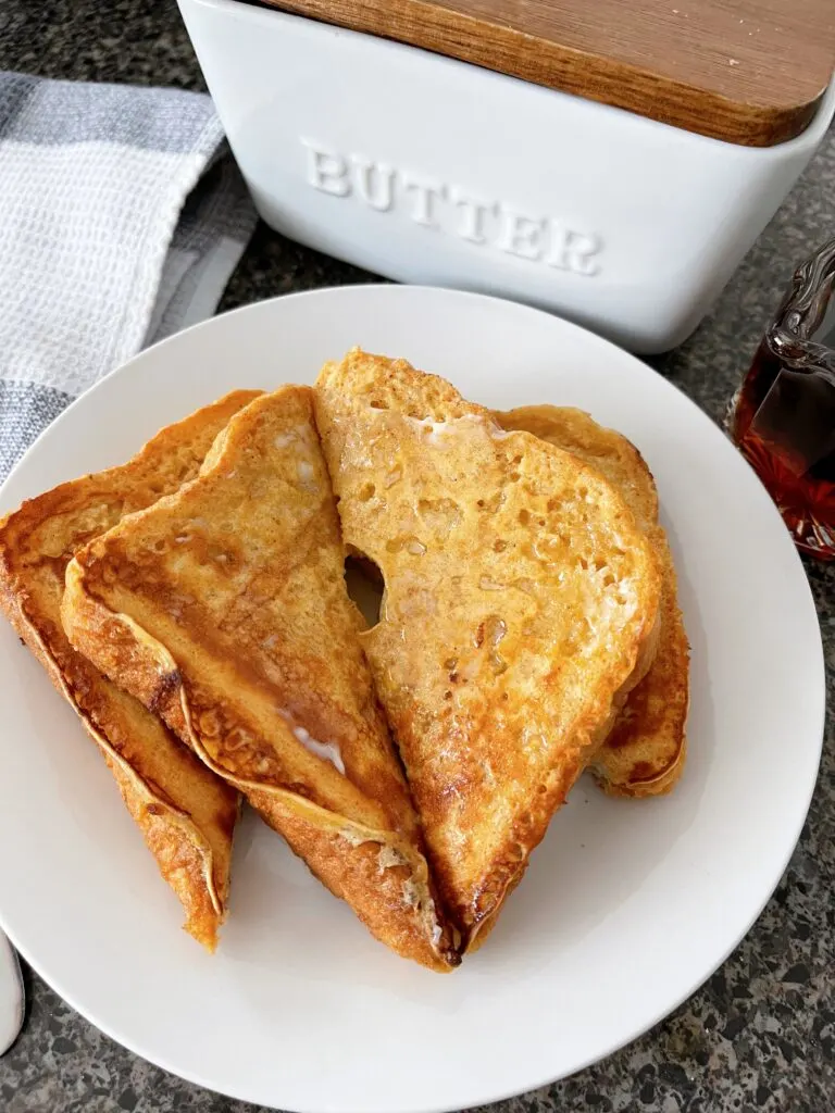 Slices of French Toast on a white plate with butter and syrup.