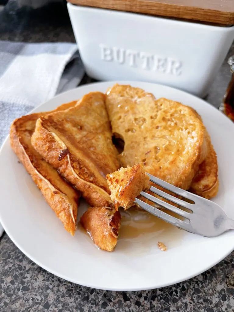 A fork with two slices of french toast topped with syrup.