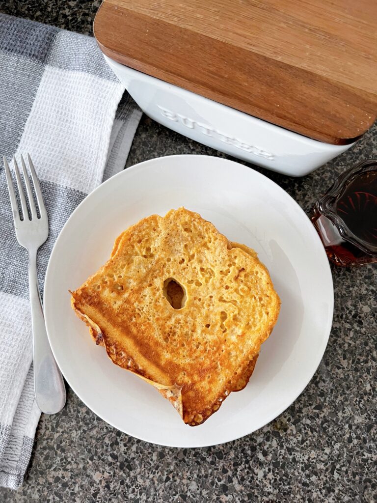 French toast on a plate with a fork, butter, syrup, and towel.