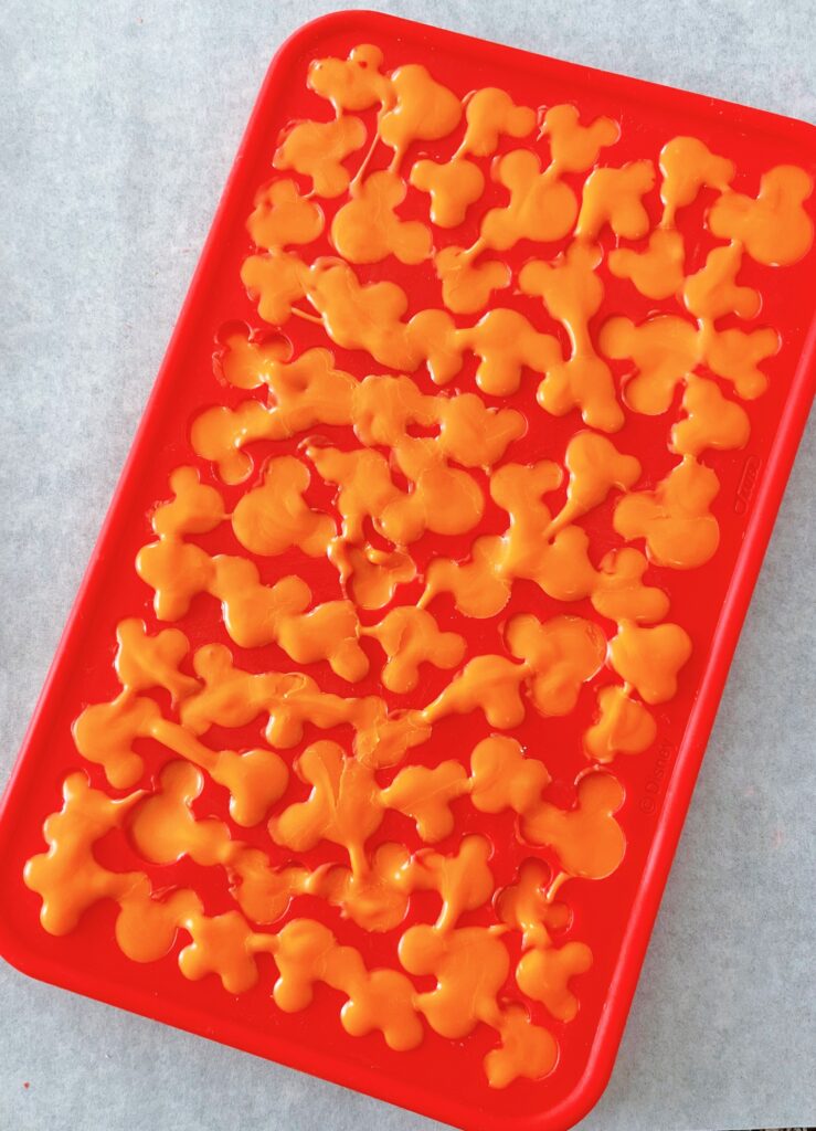 Orange candy melts that have hardened in a Mickey Mouse silicone mold.