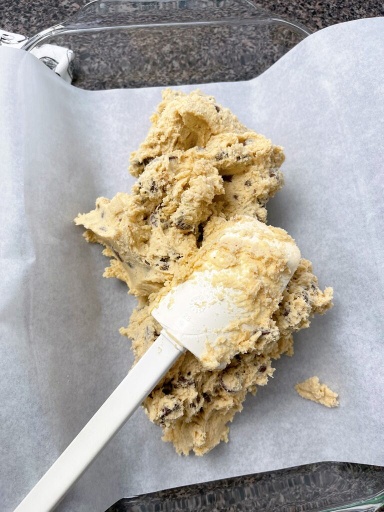 Cookie dough being spread in a 9x13 pan.
