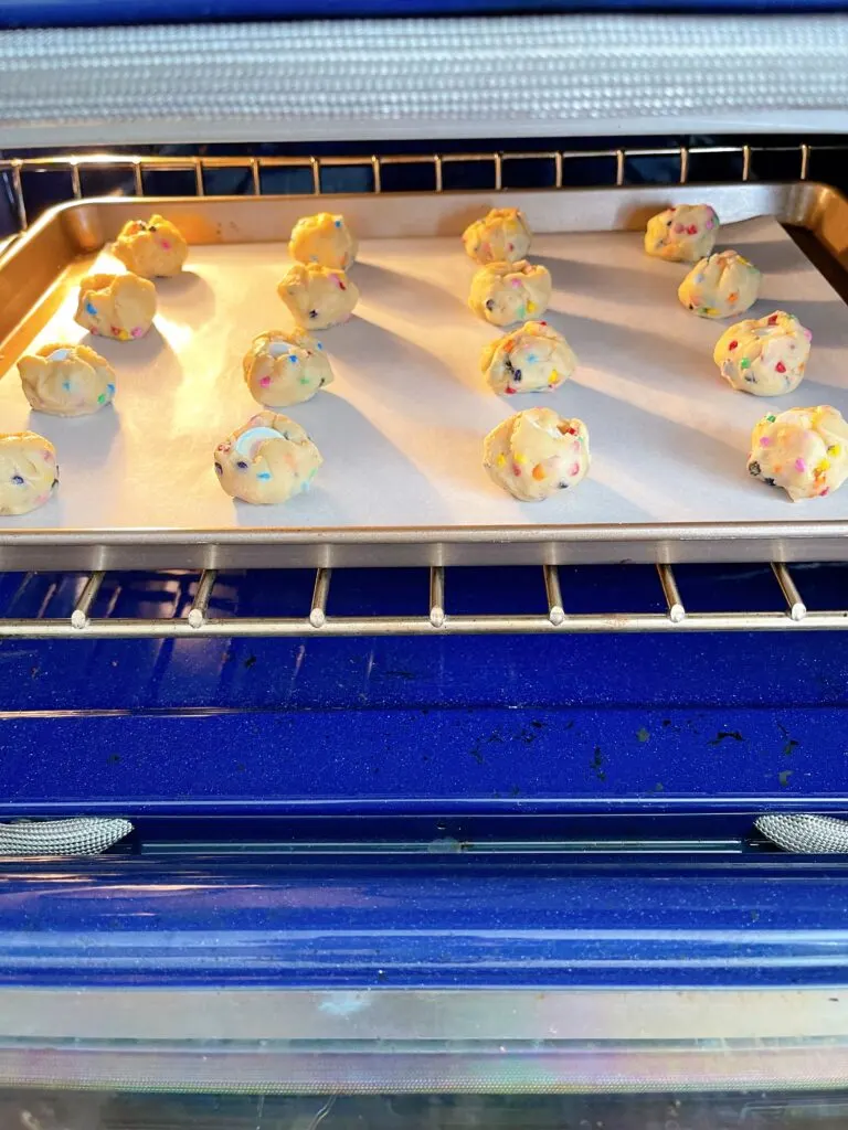 Rainbow Chip cookie dough balls on a baking sheet in an oven.
