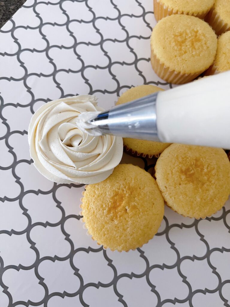 White frosting being piped onto a vanilla cupcake to make a cupcake dress.