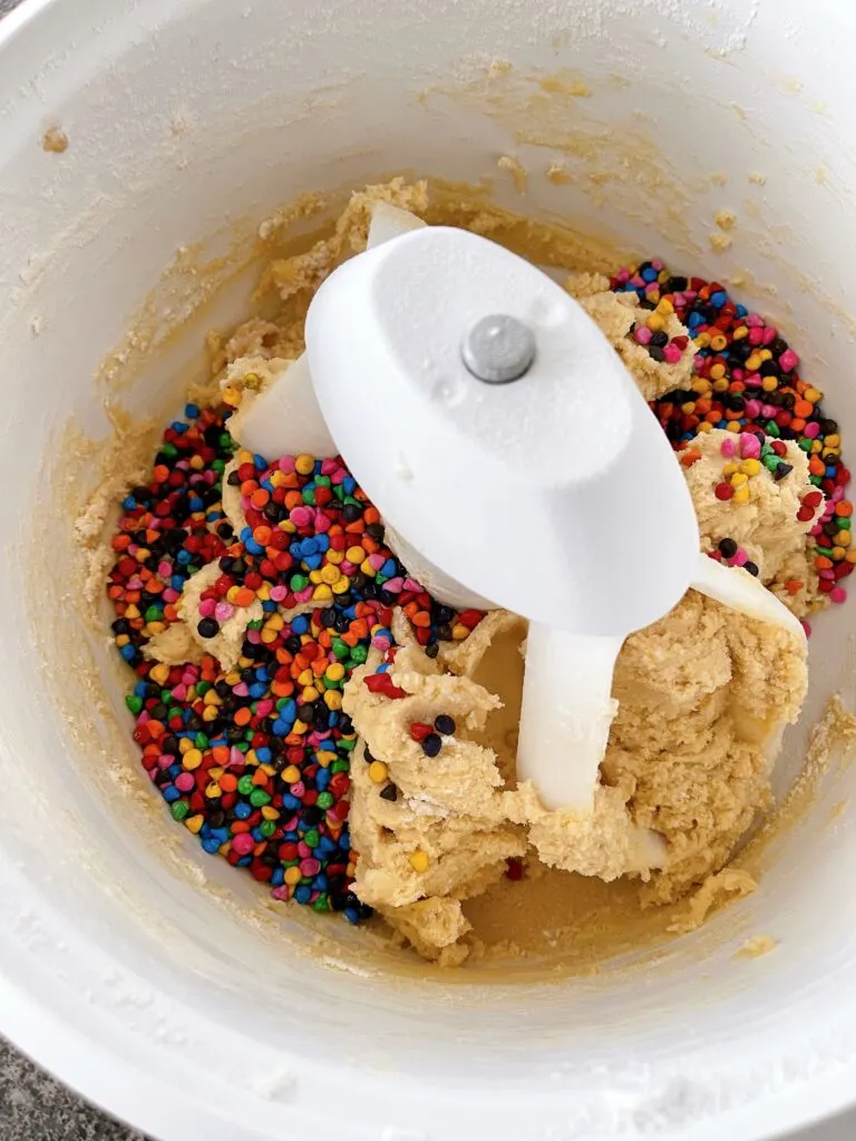 Cookie dough an rainbow chips in the bowl of a stand mixer.