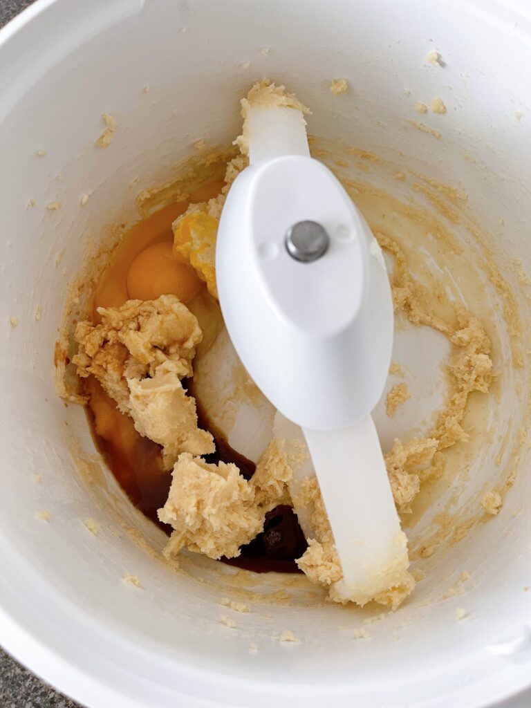 Eggs and vanilla extract with cookie dough in the bowl of a stand mixer.