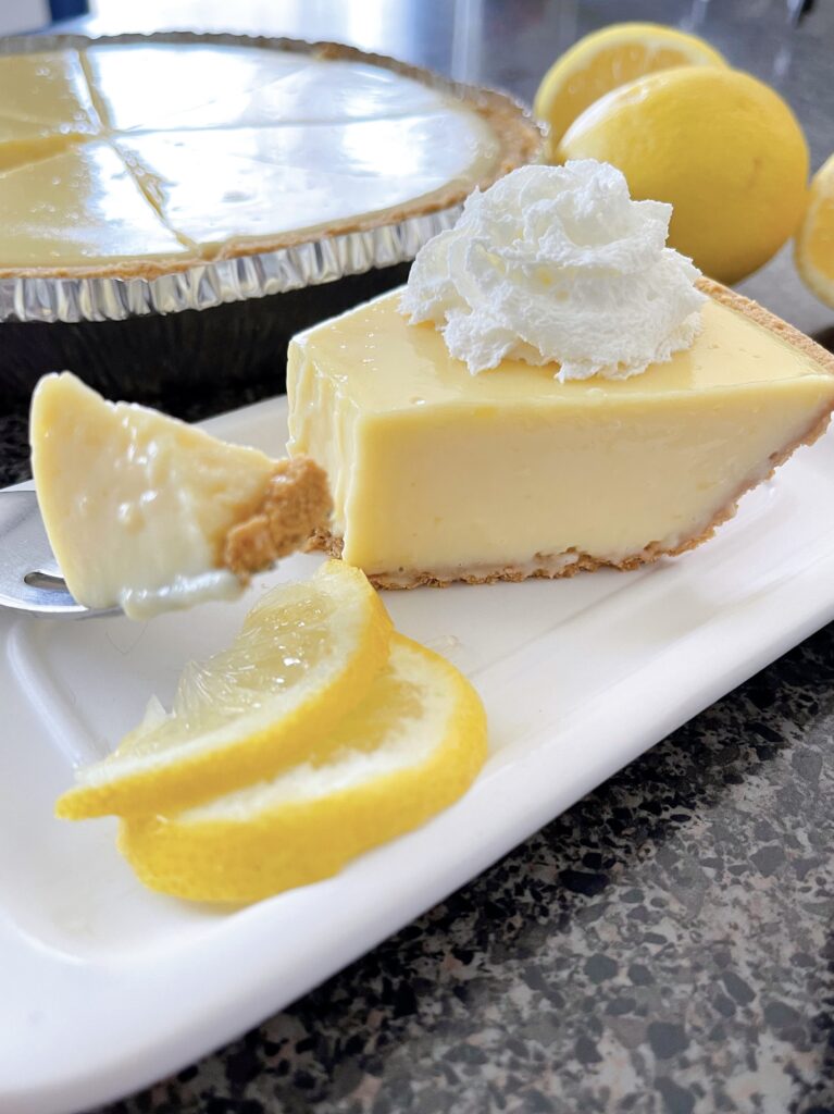 A slice of easy lemon icebox pie on a plate with two lemon wedges.