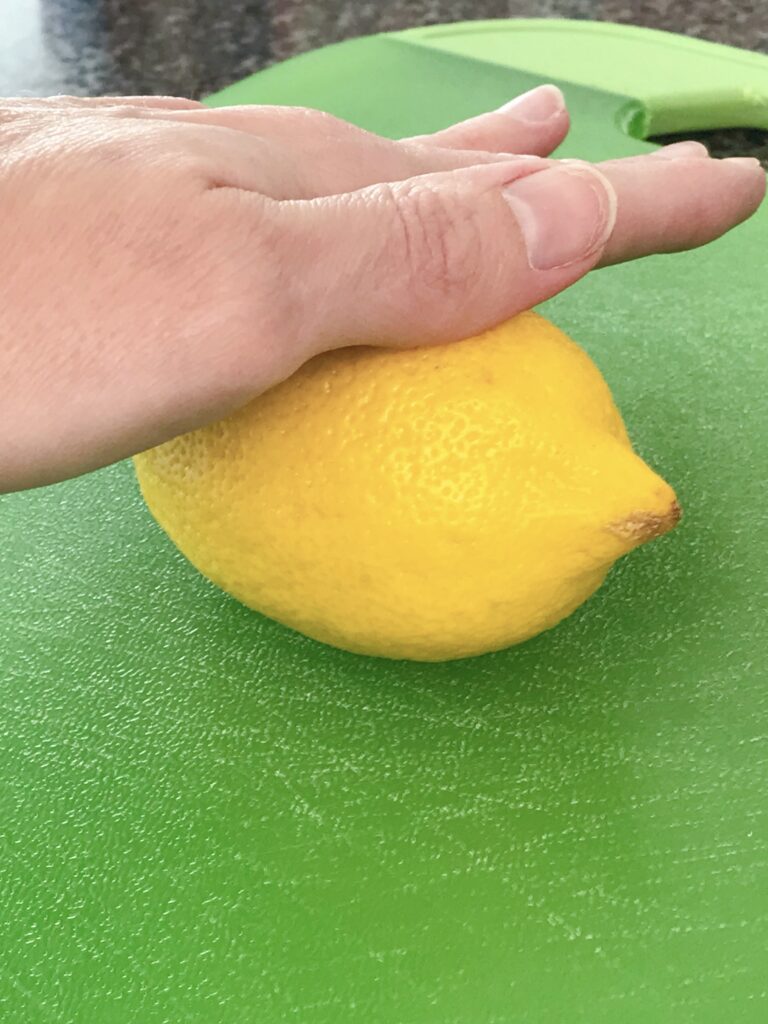 A hand rolling a lemon on a green cutting board.