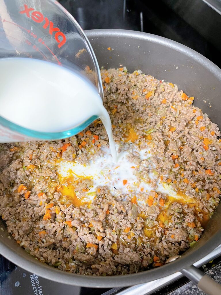 Milk poured into a pan of Bolognese sauce ingredients.