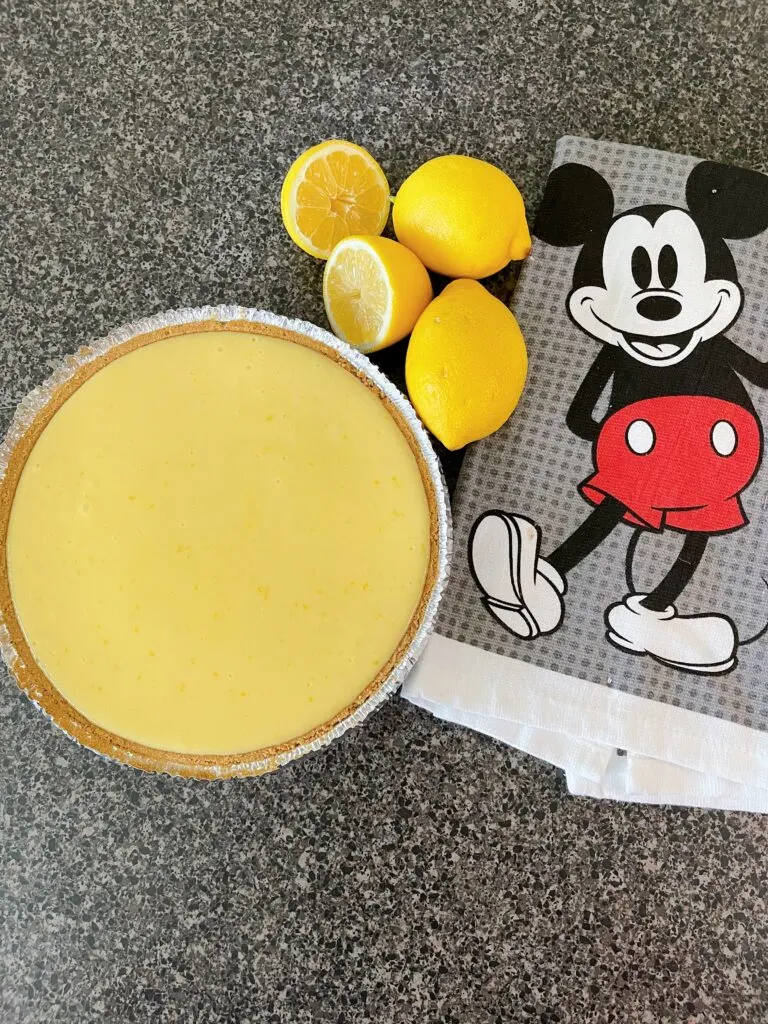 Freshly baked lemon icebox pie with lemons and a Mickey Mouse towel.