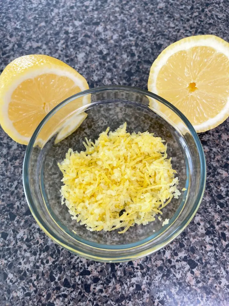 Lemon zest in a bowl with two sliced lemons.