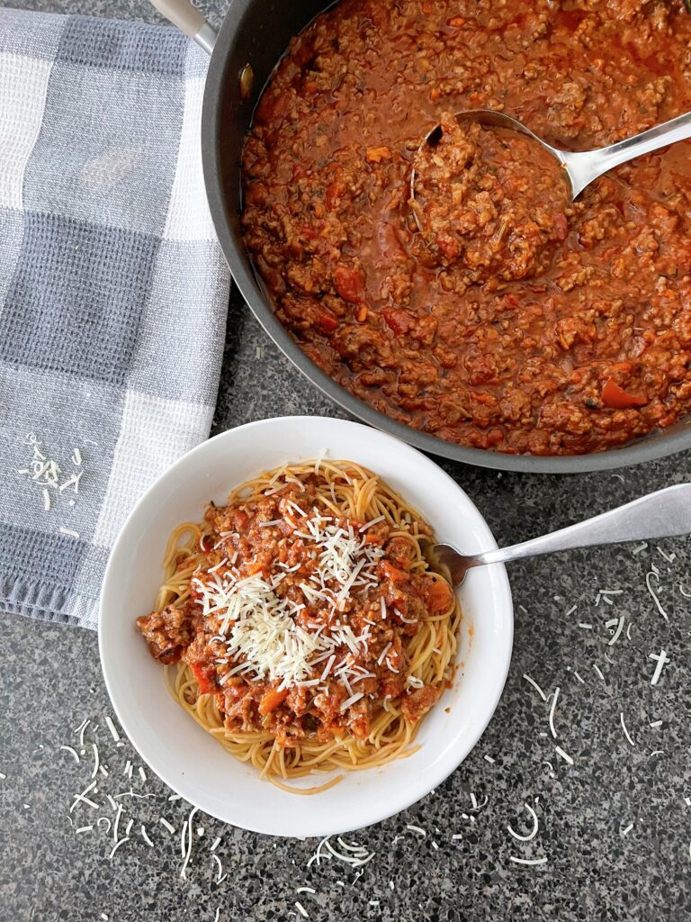 A bowl of spaghetti Bolognese and a pan of sauce.