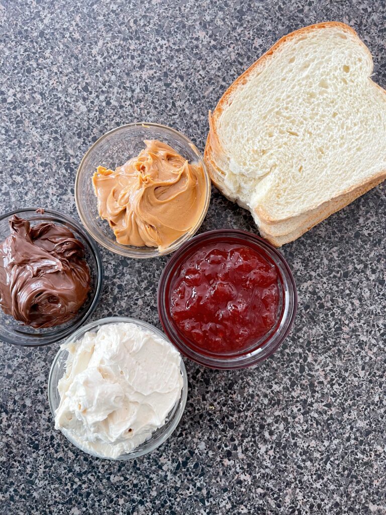 Slices of bread with peanut butter, jam, Nutella, and honey butter.