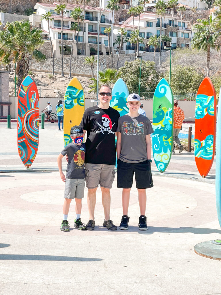 A dad and two kids in front of surf boards in Cabo San Lucas Mexico.