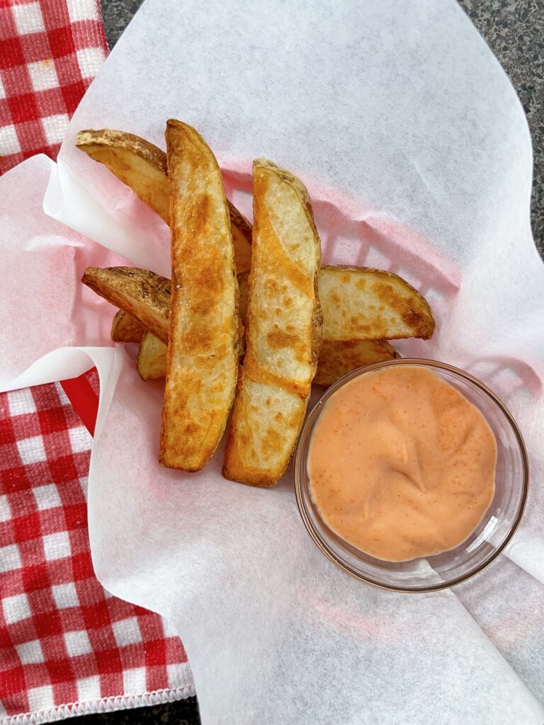 Air fryer potato wedges and fry dipping sauce in a red basket with parchment paper.