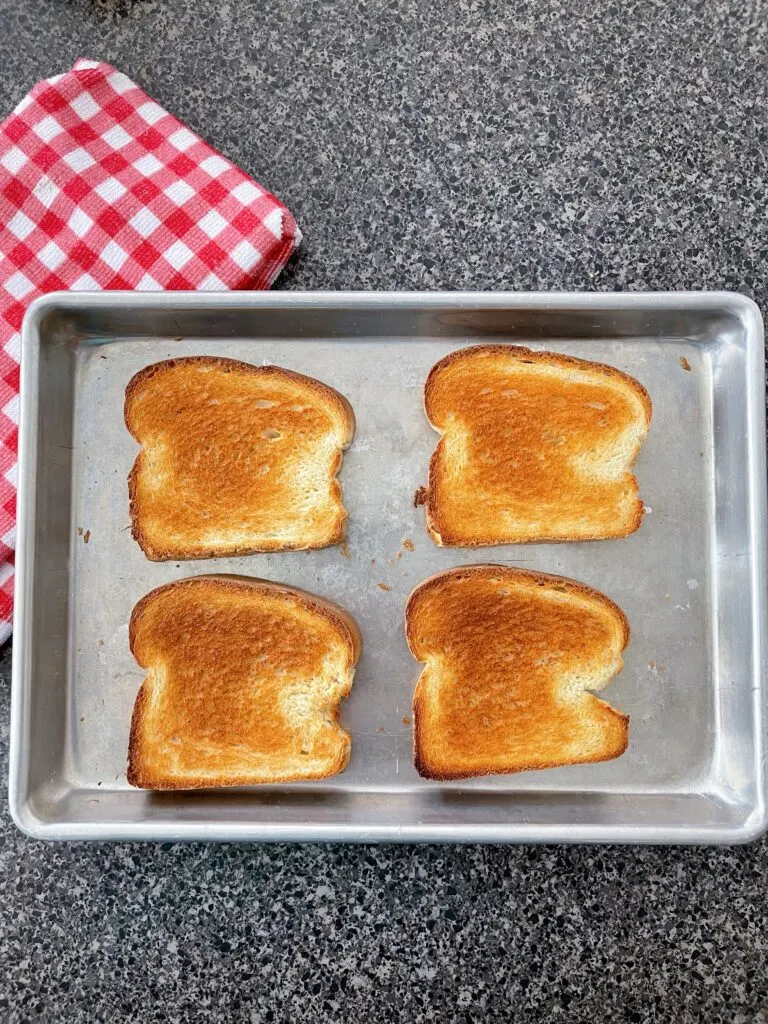 Four slices of oven toast on a baking sheet.