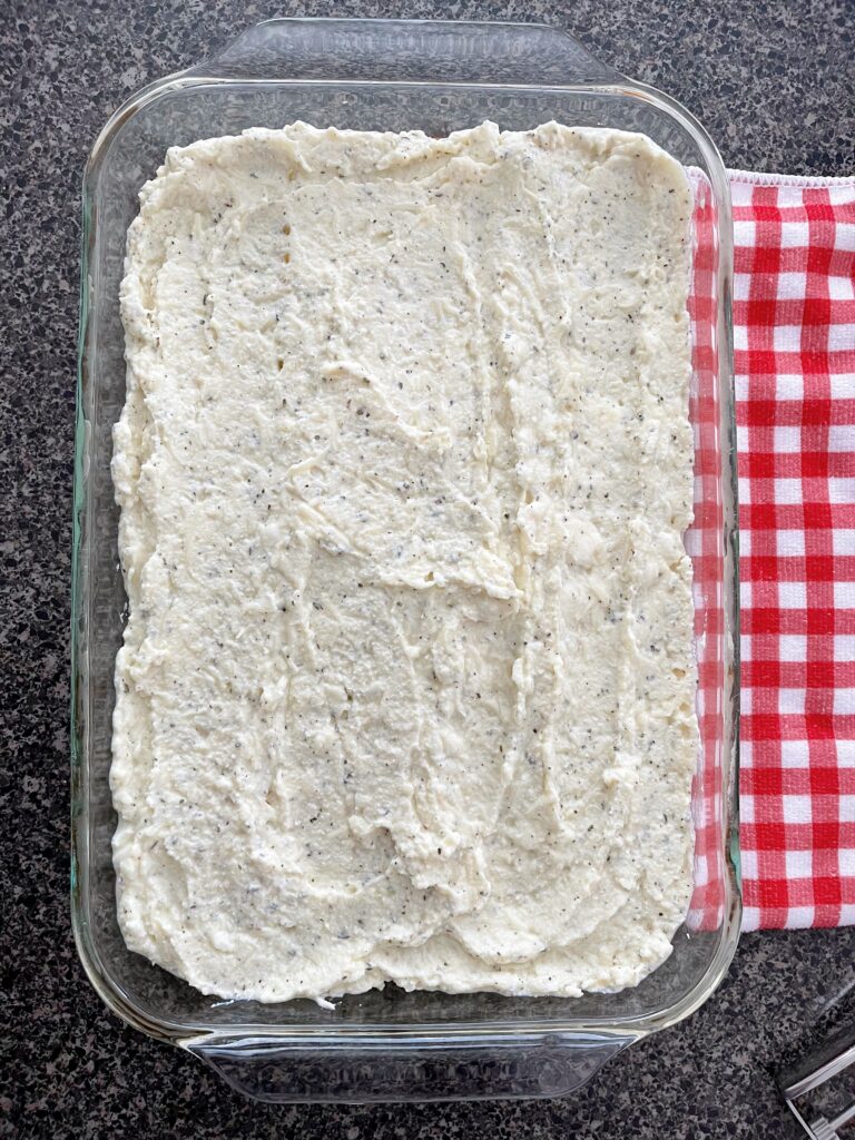 Layers of lasagna noodles in a baking dish topped with ricotta and pasta sauce.