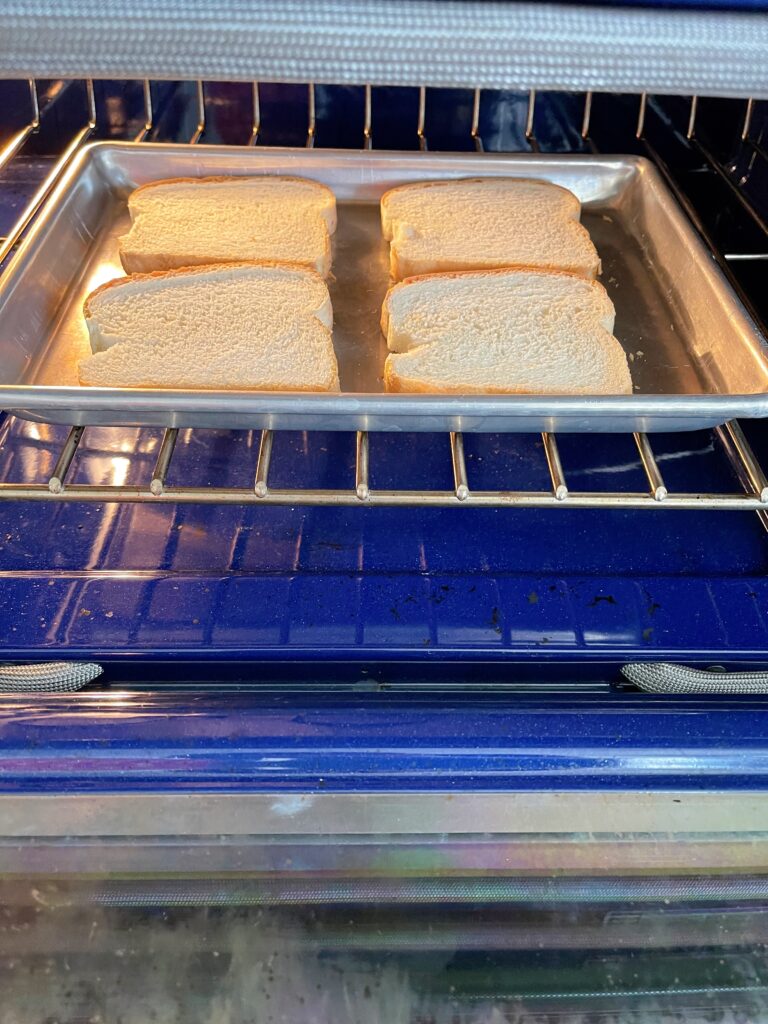 Four slices of bread on a baking sheet to be toasted in the oven.