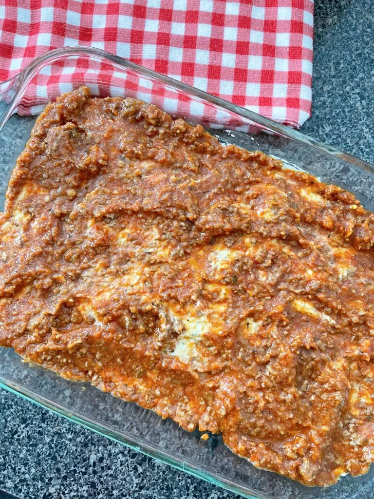 Layers of lasagna noodles in a baking dish topped with ricotta and pasta sauce.