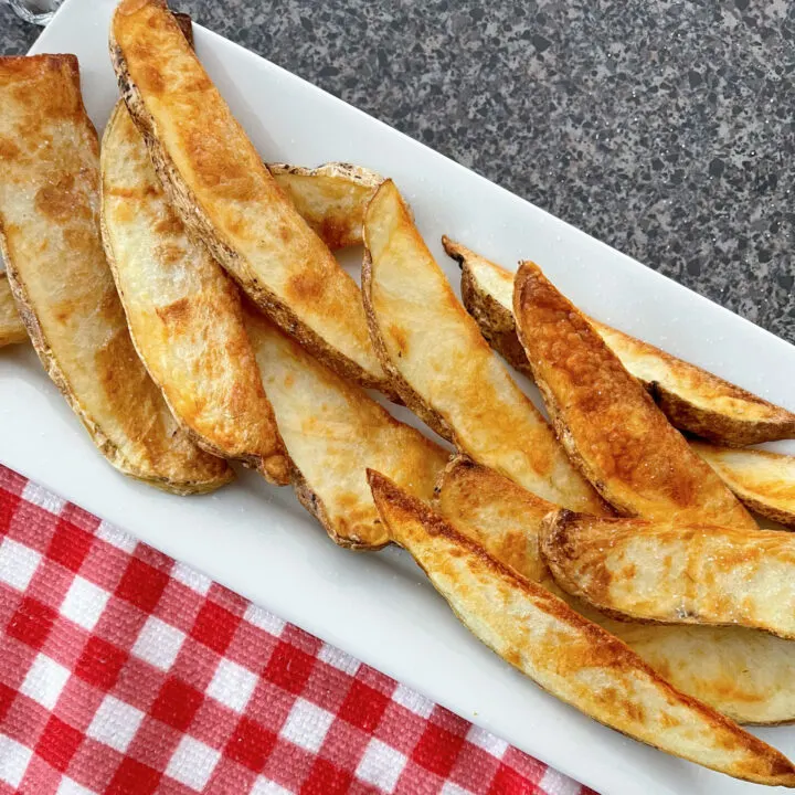 Picture of air fryer potato wedges on a white plate with a red and white towel.